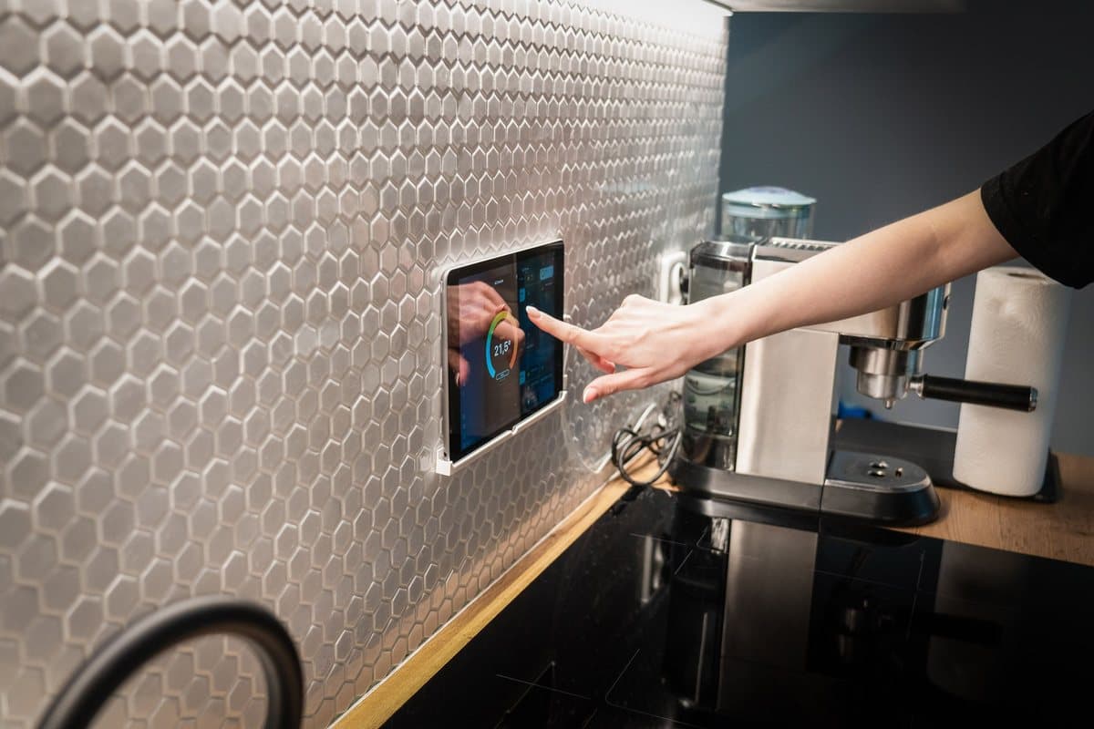 A hand using a touchscreen panel mounted on a kitchen wall